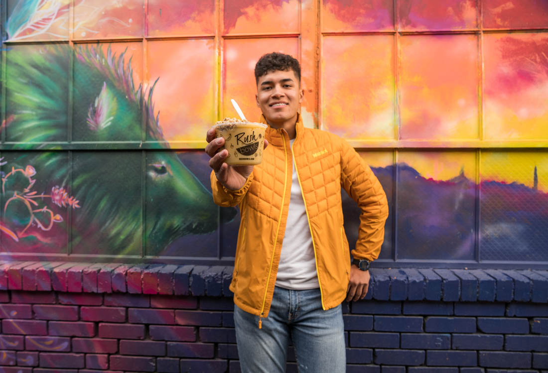 A man holding a Rush Bowls in front of an acai bowl & smoothie franchise location!